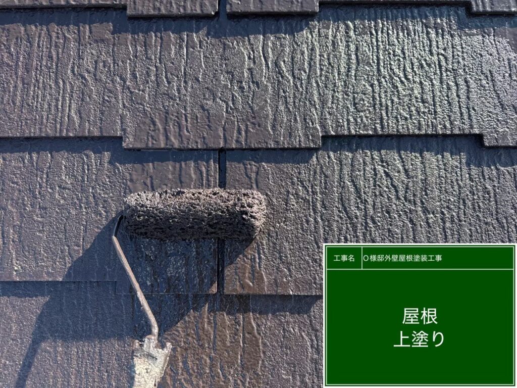 【屋根 スレート瓦上塗り施工中】<br />
屋根塗装の最終仕上げとなる上塗り（3回目の塗装）を行っています。中塗り同様に贅沢な高級遮熱塗料をもう一度重ねる「計3回塗り」を徹底することで、過酷な屋根の上の紫外線や雨風からお家を長期間守り抜く肉厚な保護膜を作り上げていきます。