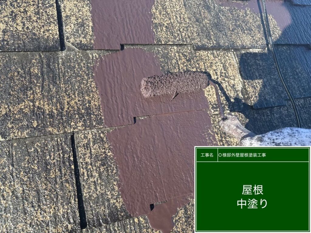 【屋根 スレート瓦中塗り施工中】<br />
下塗りが完全に乾燥した後、中塗り（2回目の塗装）を進めていきます。紫外線に強い高耐候性の遮熱塗料を使用し、屋根の重なり目や細かい部分までローラーと刷毛を使って色を均一にのせていきます。<br />
