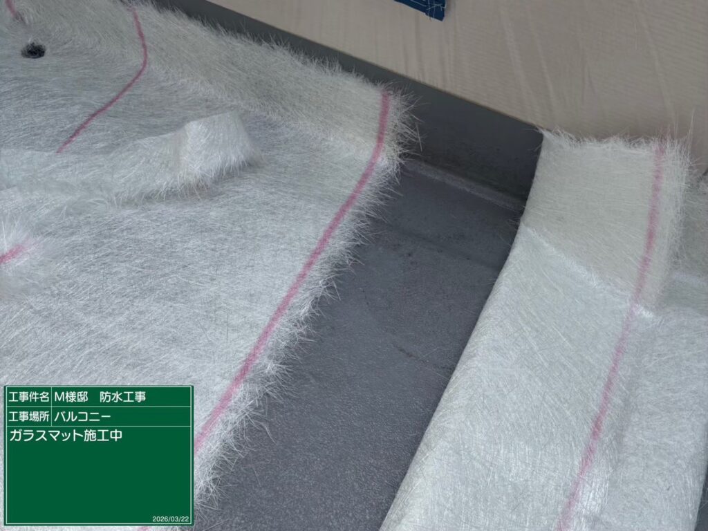 【FRP防水 ガラスマット施工中】<br />
ベランダの形状に合わせて、強靭なガラス繊維でできた「ガラスマット」を隙間なく敷き詰めていく、非常に緻密な職人技の工程です。立ち上がり部分やコーナーの隅々まで、ヨレや隙間が出ないよう正確に裁断・配置していきます。